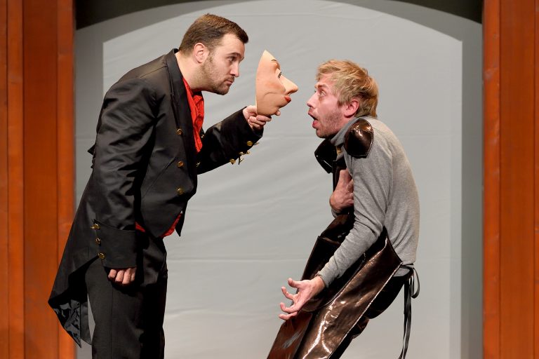 Image de la représentation "Le Magasin des Suicides" sur laquelle deux acteurs sont entrain de se disputer, l'un d'eux détenant un masque dans une de ses mains - une création de la compangie Nandi